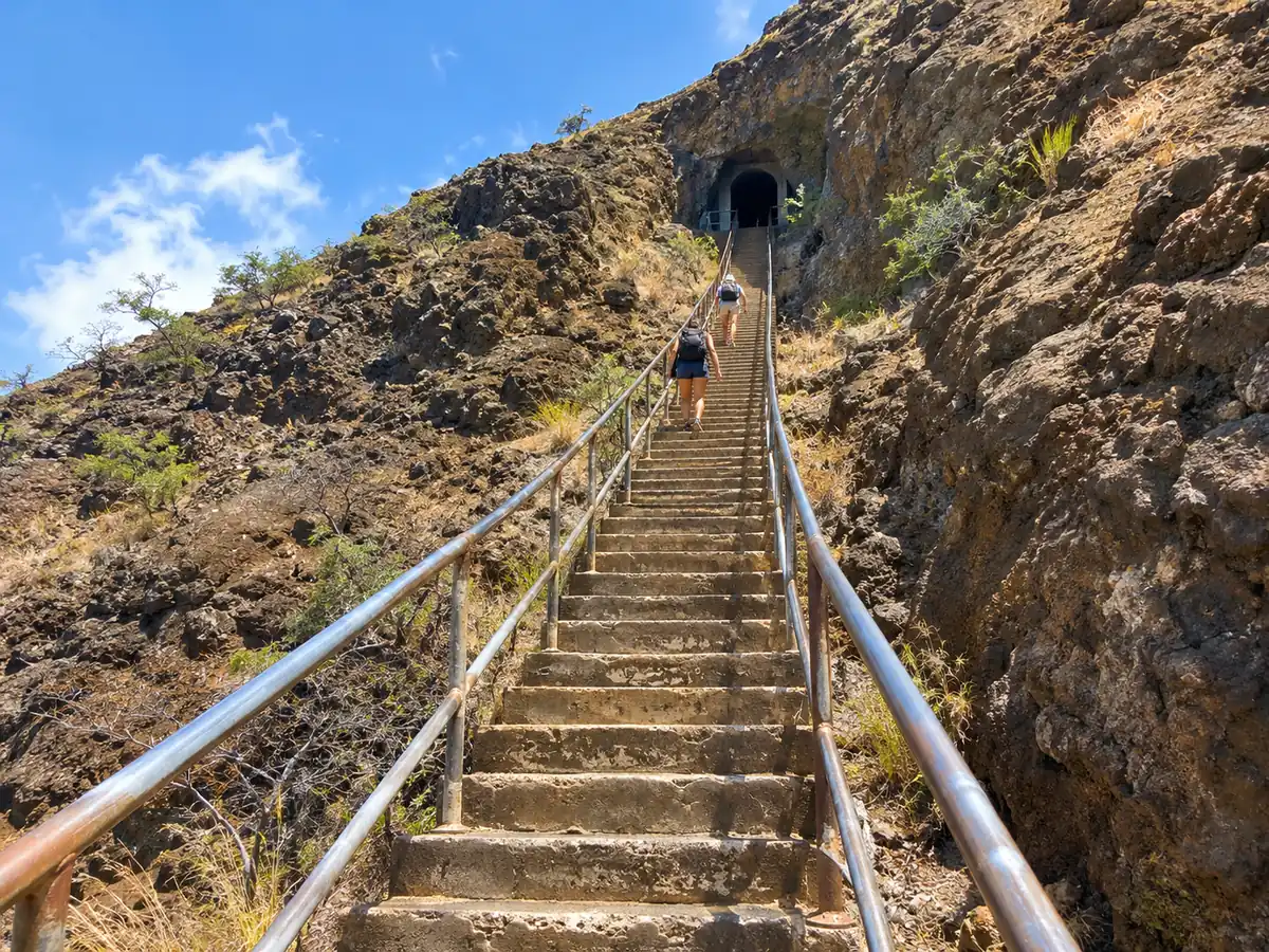 Long concrete stairs with handrails climbing toward a tunnel opening on the Diamond Head trail