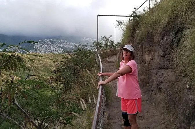 A hiker on a railed ridge path with the ocean below